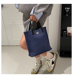 Détail du sac cabas en denim bleu avec anses en cuir noir et fermoir rotatif doré
