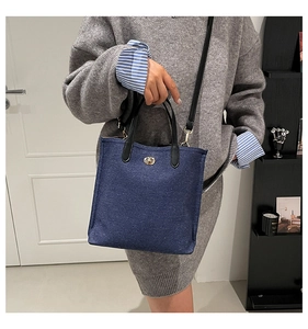 Vertical denim tote bag with gold twist lock and black leather handles shown with a model