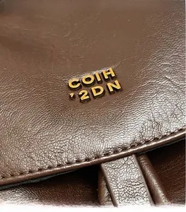 Dettaglio in macro della pelle marrone martellata con logo dorato sulla borsa