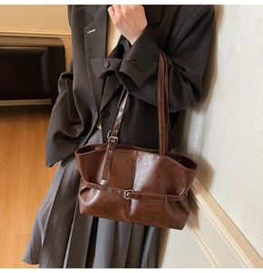 Close-up of brown textured leather tote bag featuring buckle and metal eyelet details