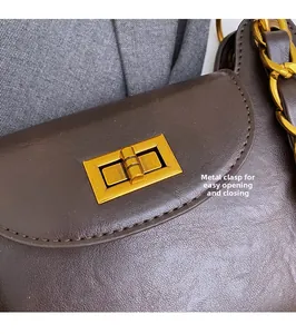 Gros plan d'un fermoir doré rotatif et d'une grosse chaîne sur un sac en cuir marron