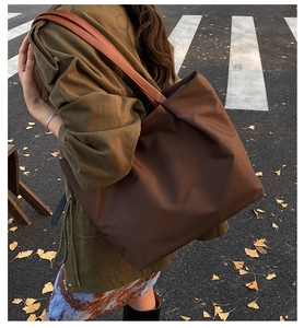 Detail of a large brown tote bag showing smooth nylon texture and leather shoulder strap