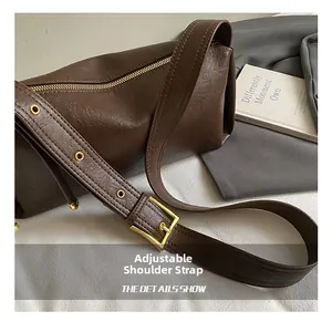 Détail de la large bandoulière réglable avec boucle en métal doré sur le sac en cuir marron