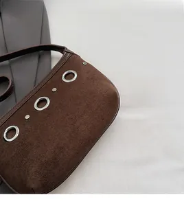 Detail of brown suede shoulder bag featuring three vintage silver metal eyelets and soft texture