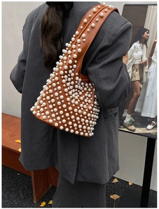 Detail der braunen Eimer-Tasche mit luxuriösen Perlennieten und breitem Gurt