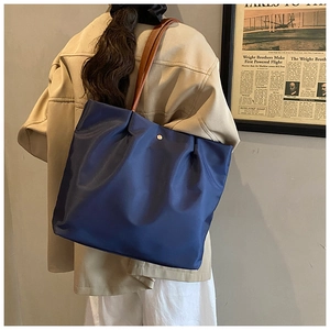 Detail of navy blue nylon tote bag with brown leather shoulder straps and gold metal snap