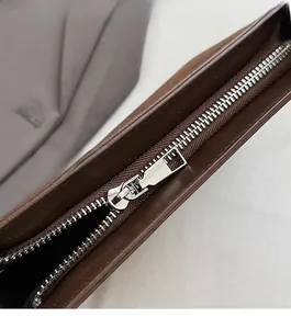 Detail of a smooth silver metal zipper on a dark brown suede handbag with neat stitching