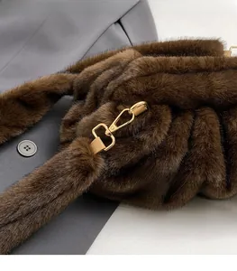 Détail de la boucle en métal doré et de la bandoulière en peluche marron du sac seau