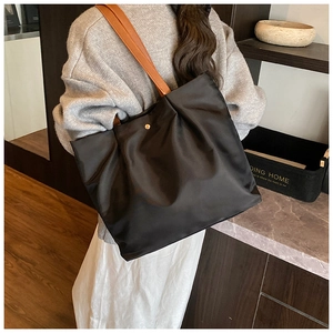 Detail of large black nylon tote bag with brown leather straps shown on shoulder