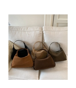Detail view of five suede hobo bags in assorted earthy colors on a white sofa