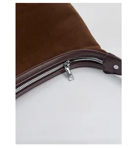 Detail of silver metal zipper and dark brown suede texture on a chic shoulder bag