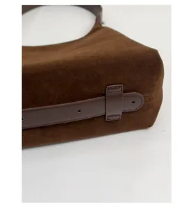 Detail of wide bottom design and perforated leather strap on brown suede tote bag