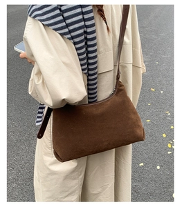 Brown suede crossbody bag worn with a beige trench coat in an autumn street setting