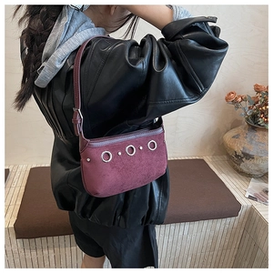 Detail view of burgundy suede underarm bag featuring three silver metal rings on a model