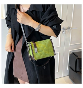 Detail of green quilted crossbody bag with brown trim and silver lock on black coat
