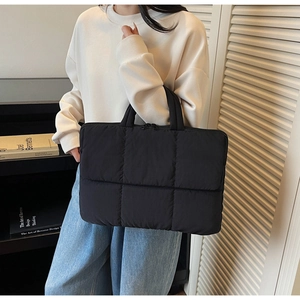 Detail of a black quilted laptop tote bag with square puff texture and sturdy handles