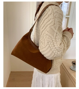 Close-up of brown suede hobo bag styled with a beige sweater and white pleated skirt