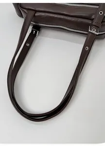 Detail of dark brown leather shoulder bag showing metal hardware and dual zipper closure