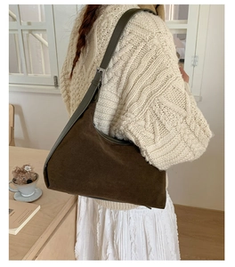 Detail of dark brown suede shoulder bag with adjustable strap on a cream knit sweater