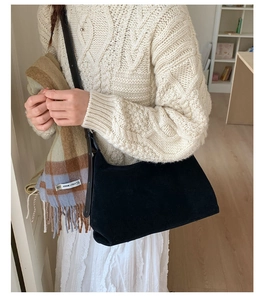 Detail of a minimalist black suede shoulder bag paired with a white cable-knit sweater