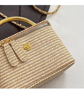 Detail of woven cream mini box bag featuring golden metal handle and camellia logo