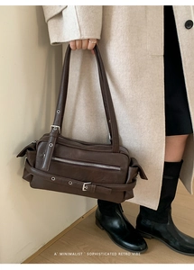 Detail of vintage brown leather pillow bag featuring metallic zippers and decorative belts