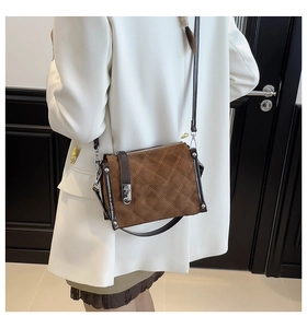 Detail of a brown quilted crossbody bag with a silver metal twist lock on a white blazer