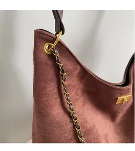Close-up of brown suede shoulder bag featuring a gold chain detail and metallic lock