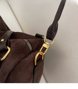 Gros plan détaillé des attaches métalliques dorées sur ce sac à bandoulière en daim brun