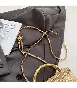 Detail of woven cylinder bag with gold metal handle and decorative golden ball chain