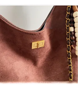 Close-up of golden metal clasp on brown suede shoulder bag with chain strap and beads