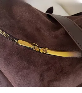 Détail de la fermeture éclair dorée sur un sac cabas en daim marron foncé avec bandoulière
