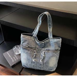 Detail of light blue washed denim tote bag showing dual zipper pockets and pull cords