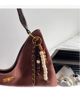 Detail of caramel suede bag with gold square clasp and decorative beaded chain charm