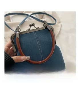 Detail of blue denim crossbody bag with vintage bronze kiss-lock and brown ring handle