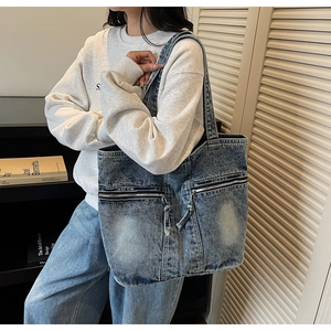 Detailed view of blue denim tote bag with dual zipper pockets on a female model