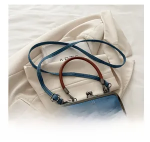 Close-up of denim bag with white stitching, leather handle and metal clasp closure