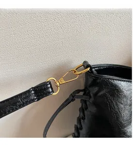 Detailansicht der schwarzen Lackledertasche mit goldenen Karabinerhaken und D-Ring-Beschlägen