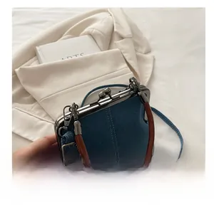 Close-up of retro metal clasp and denim texture on crossbody frame bag with handle