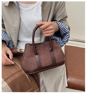 Detail of dark brown suede tote bag with leather piping and metal buckle accents