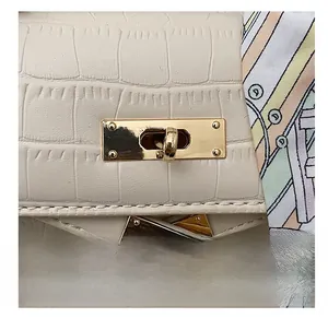 Macro shot of white crocodile embossed leather bag with gold hardware and silk scarf