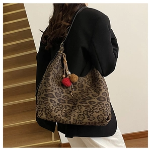 Close-up of a large leopard print tote bag with red and brown fuzzy pom-poms on the strap