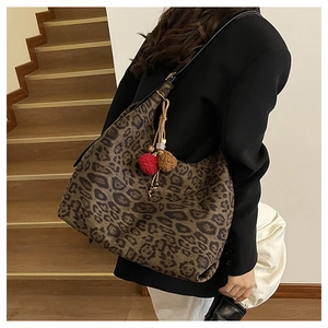 Detail view of large leopard print tote bag with decorative red pom-pom keychain