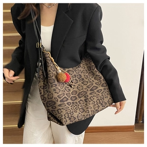 Detail of leopard print tote bag featuring a decorative pom-pom and black leather strap
