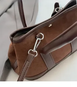 Detail of silver metal hardware and dark brown suede texture on a crossbody bag