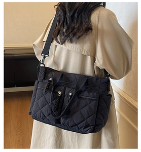 Detail of black quilted tote bag with multi-pocket structure and wide fabric shoulder strap