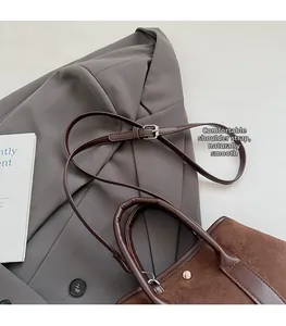 Detail of brown suede tote with leather straps and metal rivets on a grey suit background