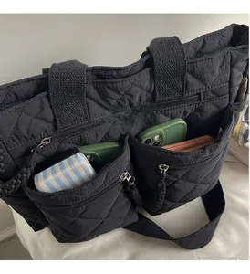 Detail of black quilted nylon tote showing functional front zipper pockets for storage