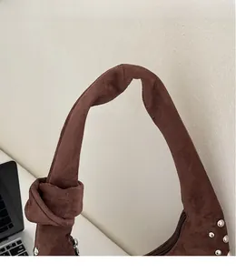 Detail of knotted shoulder strap on brown suede bag with silver rivet accents