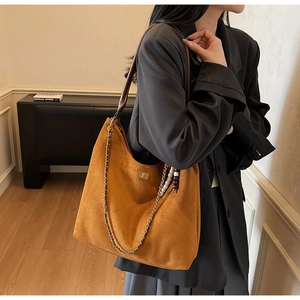 Detail of brown suede tote bag with chain strap and bead charms shown on shoulder